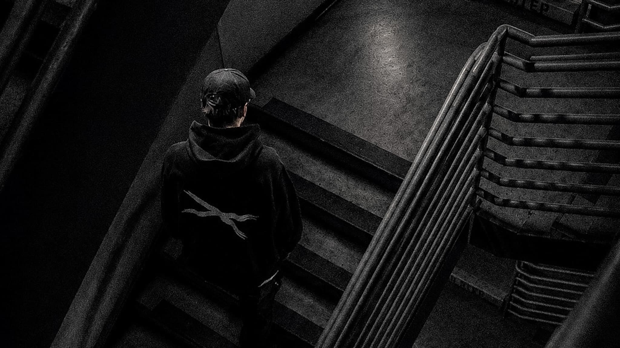 Overhead view of a figure on a stairwell landing, No EviL cross on the back of a hoodie
