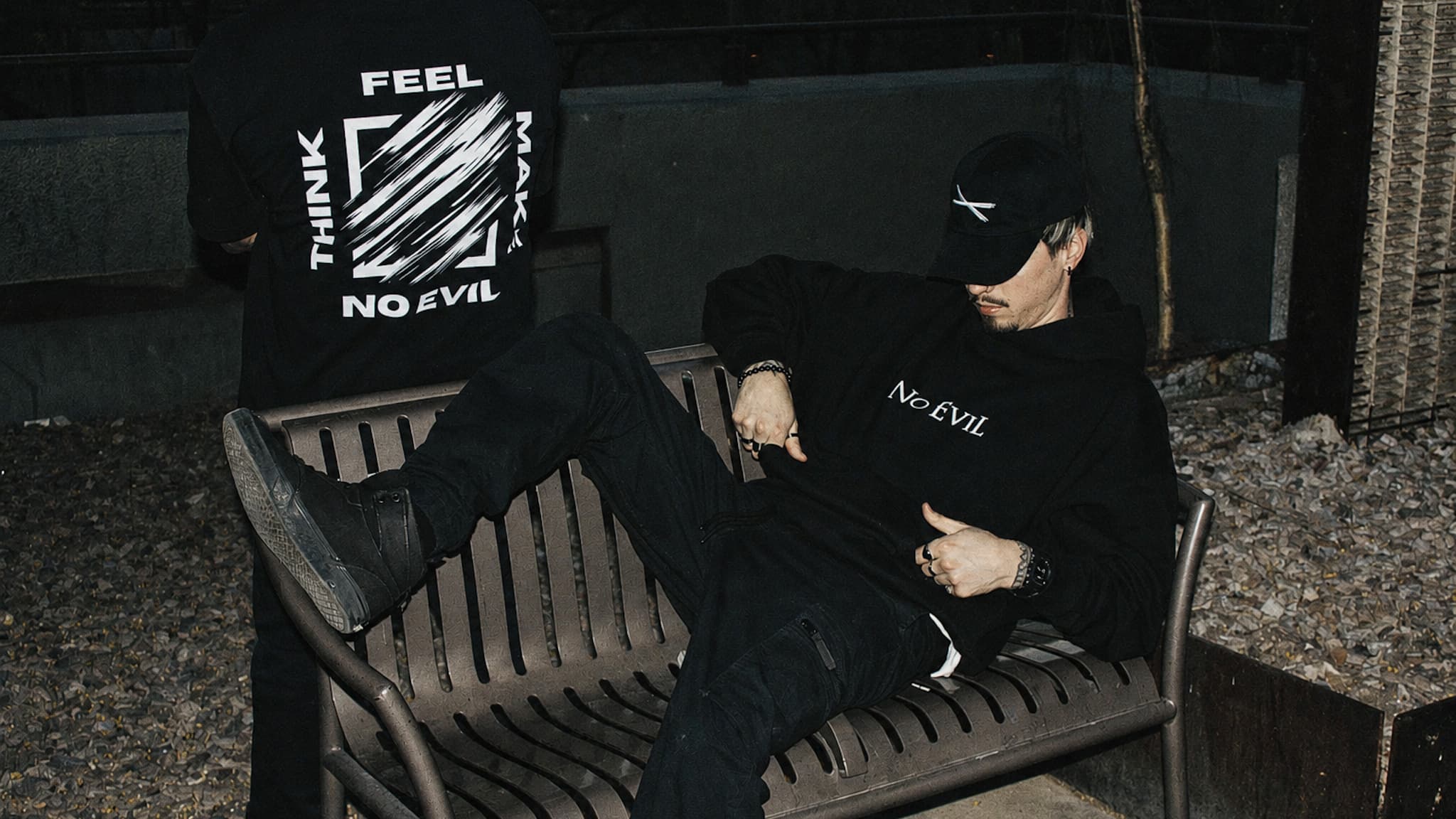 Back graphic tee and No EviL hoodie worn together on a gravel bench at night
